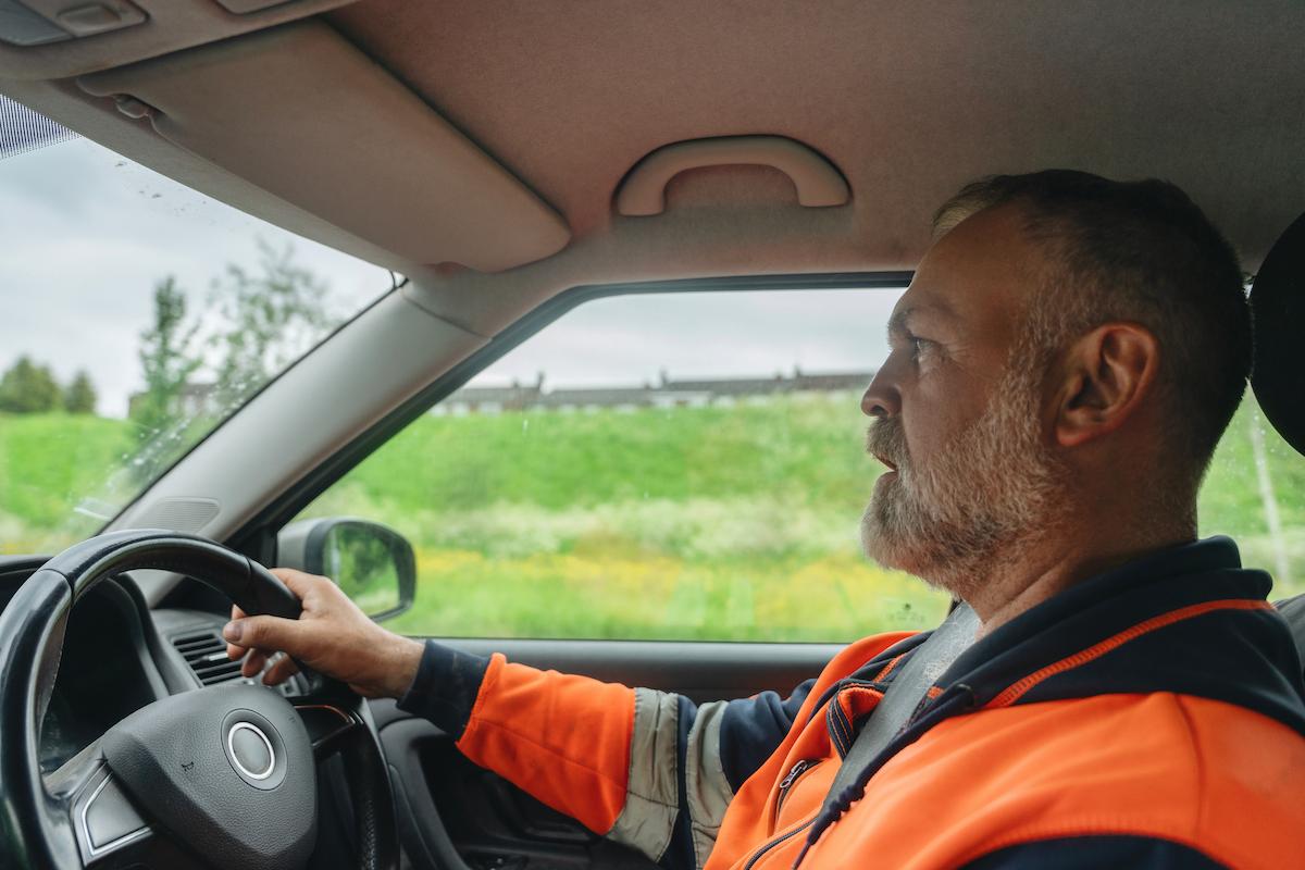Person driving a car while wearing a high‑visibility jacket.