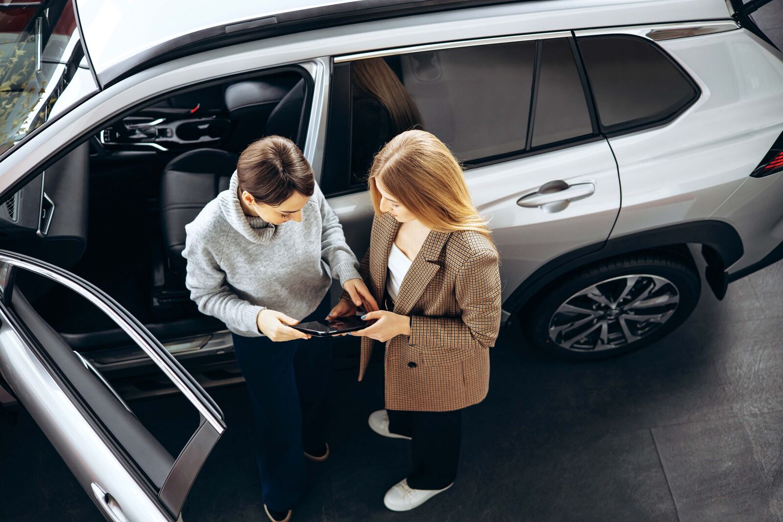 Two people working on tablet in front of a car