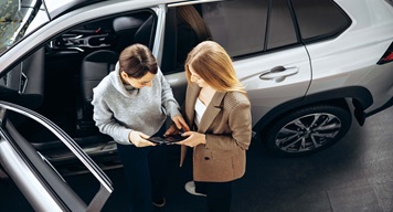 Two people working on tablet in front of a car