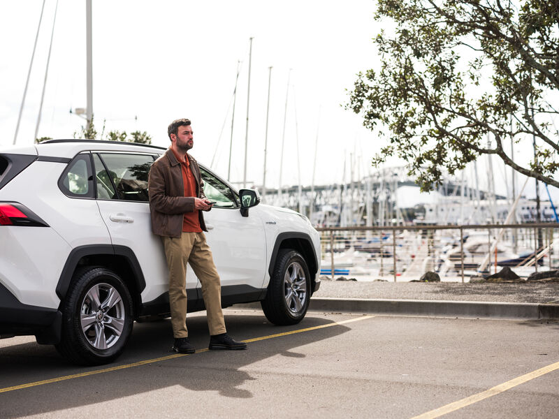 Vehicle leasing and management Man standing beside a white SUV with the Auckland Harbour Bridge in the background, showcasing fleet vehicle lifestyle and mobility