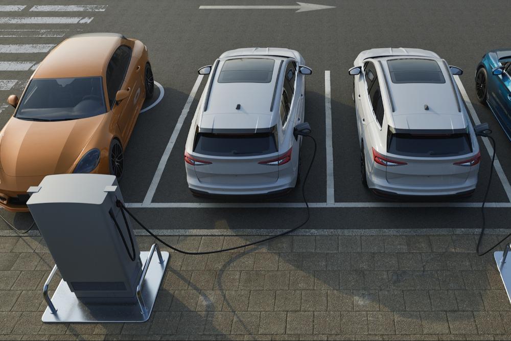 EV production UK EV production UK An aerial view of electric vehicles parked in charging bays, connected to charging points via cables.