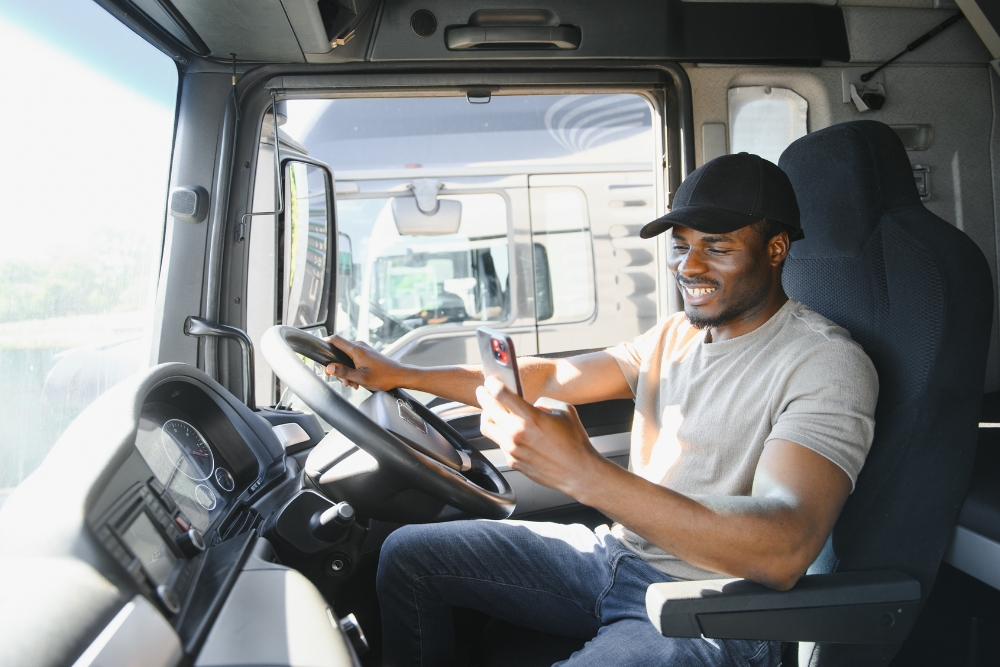 Fleet communication: Lorry driver sitting in a truck cab, smiling while using a smartphone, representing modern fleet communication and connected drivers.