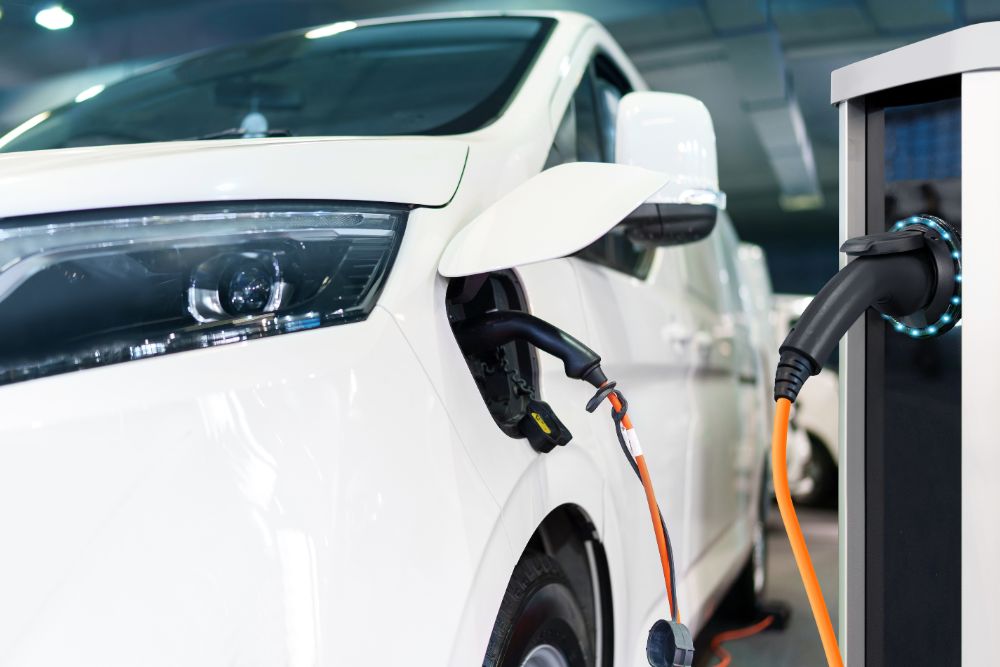 Grey fleet duty of care risks in the UK Grey fleet duty of care risks in the UK: A close-up of an orange charging cable connected to the charge port of a white electric vehicle at a charging station.