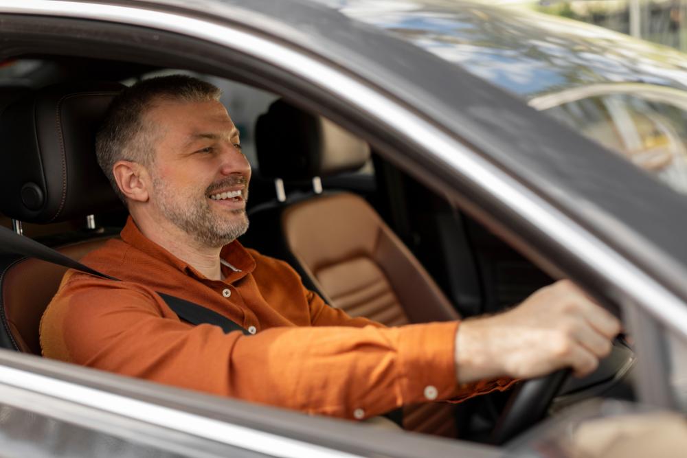 Hot weather commuting tips Hot weather commuting tips A smiling man driving a car with the window down, wearing an orange shirt.