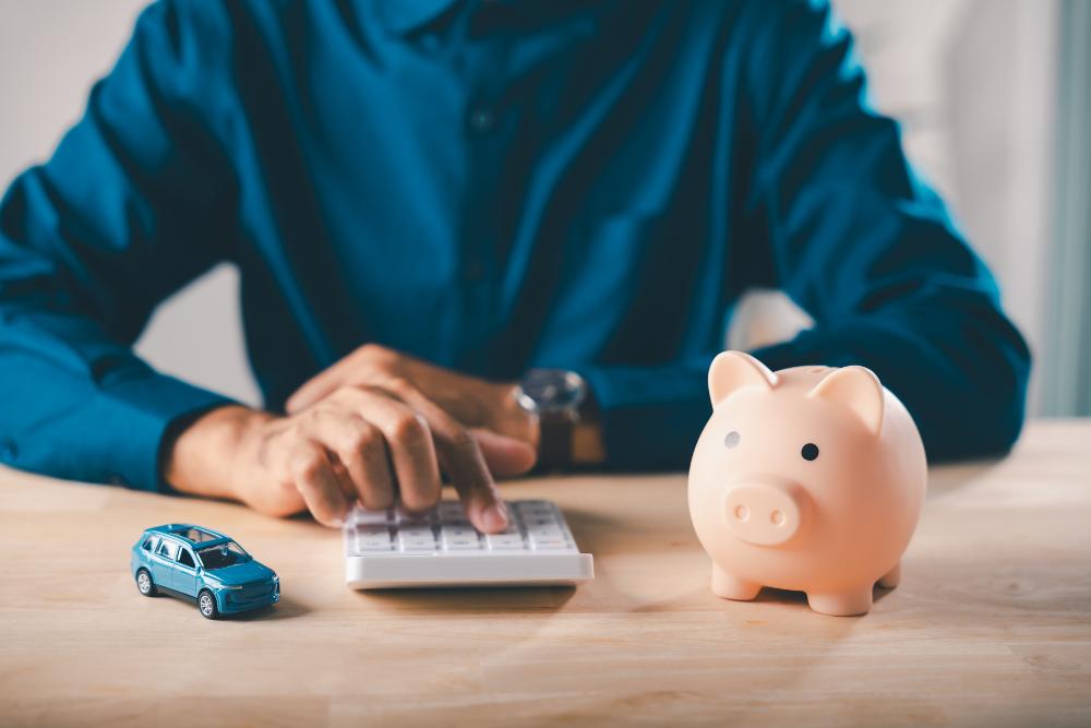 How do I report a company car on a P11D form UK How do I report a company car on a P11D form UK: A man in a blue shirt using a white calculator at a wooden desk, with a small blue toy car on one side and a pink piggy bank on the other.