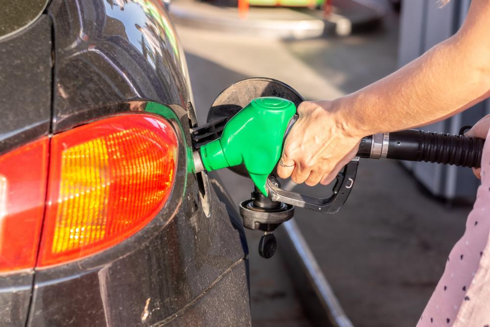 How salary sacrifice reduces commuting costs for employees: A close-up of a person's hand holding a green fuel nozzle inserted into the fuel cap of a dark-coloured car at a petrol station.