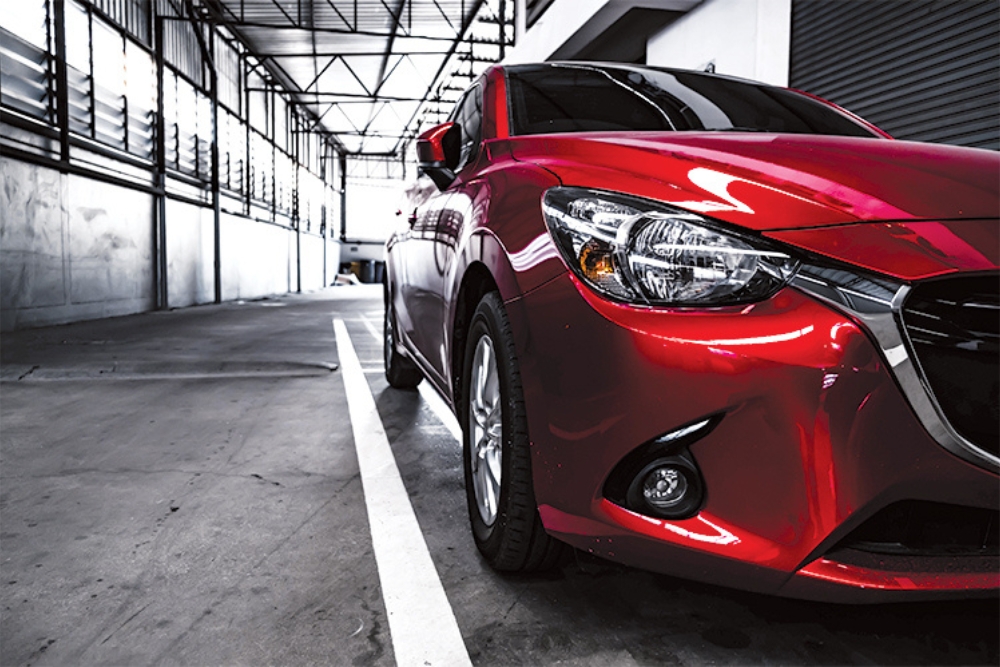 Front three-quarter view of a shiny red compact car parked inside a bright industrial garage or warehouse, emphasizing semiconductor technology.