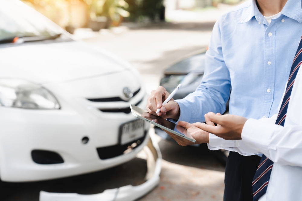 Reducing fleet admin with automation: Person standing beside a car, holding a tablet and writing notes, representing vehicle inspections or fleet administration tasks.