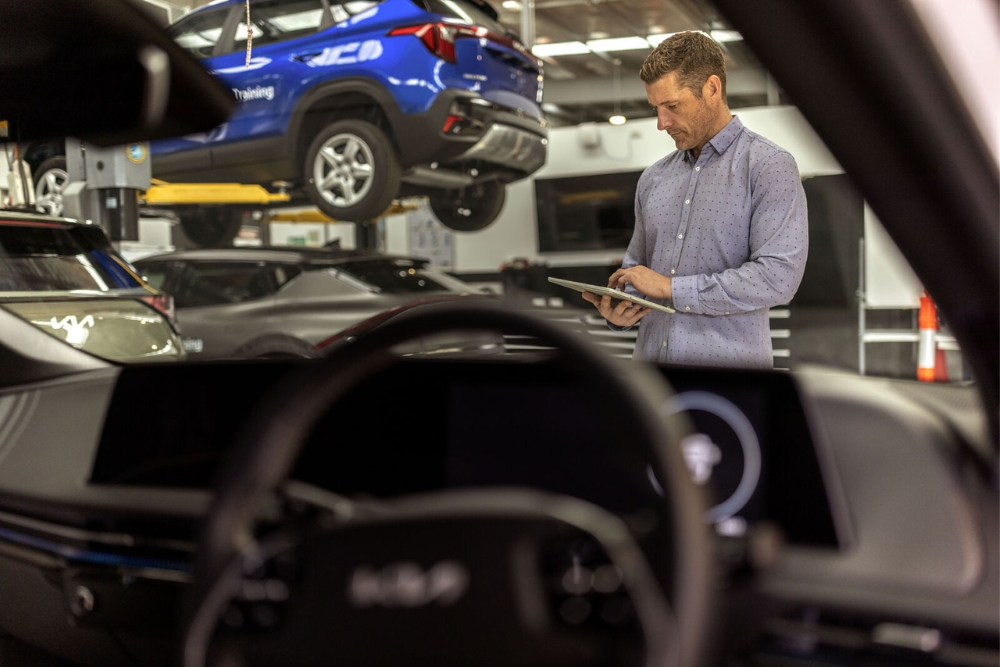An automotive technician in a workshop holds a tablet and inspects multiple cars elevated on hydraulic lifts, showcasing semiconductor-enabled fleet management and maintenance.