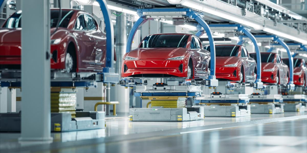 UK car production growth header image Red car bodies suspended on an automated production line inside a modern car manufacturing facility.