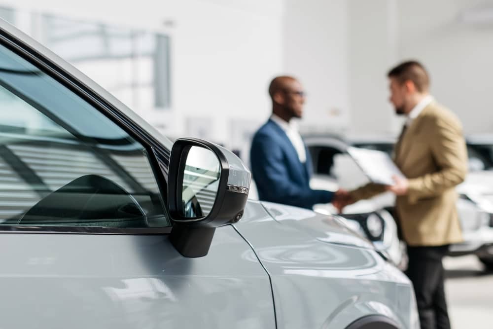 Close-up of a car with blurred background of two men shaking hands in dealership