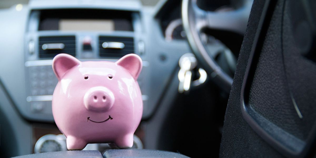 Why businesses are rethinking cash allowances: A pink smiling piggy bank sits on the centre console of a car interior, with the dashboard and steering wheel visible in the background.